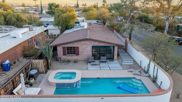 pool at dusk featuring a patio, a fenced backyard, and a pool with connected hot tub