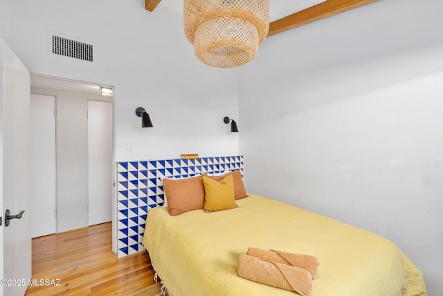 bedroom with beam ceiling, visible vents, and wood finished floors