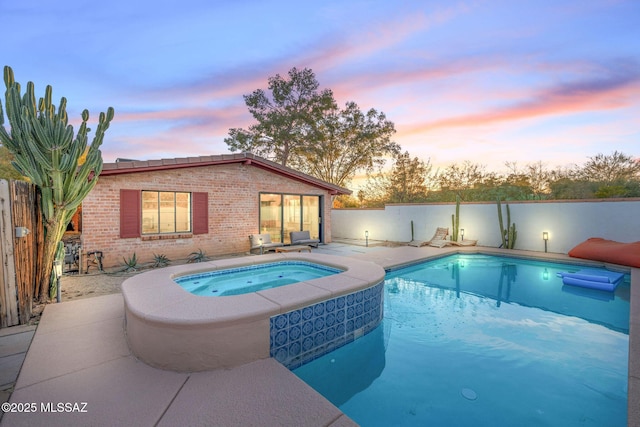 pool at dusk featuring a patio area, a pool with connected hot tub, and fence