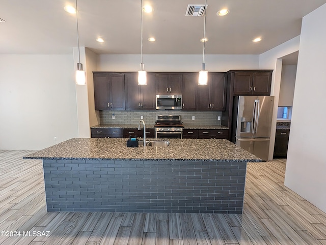 kitchen with stainless steel appliances, a center island with sink, sink, pendant lighting, and light wood-type flooring