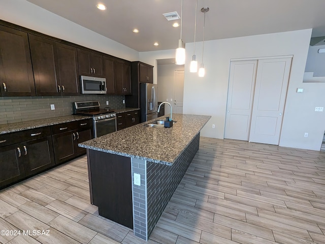 kitchen with stainless steel appliances, stone countertops, decorative light fixtures, a kitchen island with sink, and light wood-type flooring