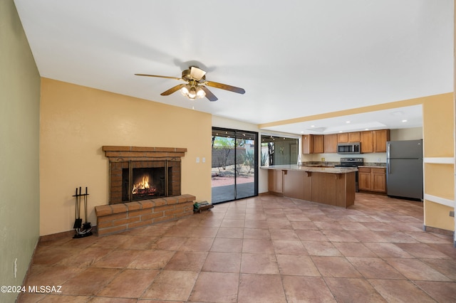 kitchen featuring a brick fireplace, kitchen peninsula, appliances with stainless steel finishes, and ceiling fan