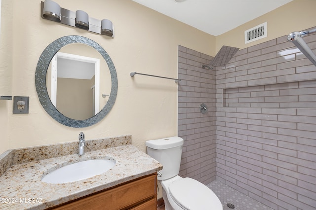 bathroom featuring vanity, a tile shower, and toilet