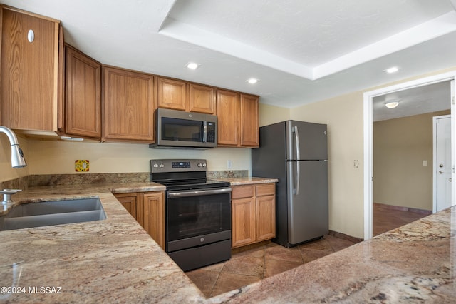 kitchen featuring stainless steel appliances, light stone countertops, sink, and a raised ceiling