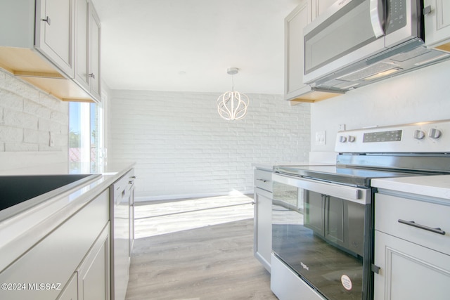 kitchen with pendant lighting, stainless steel appliances, brick wall, and light hardwood / wood-style flooring