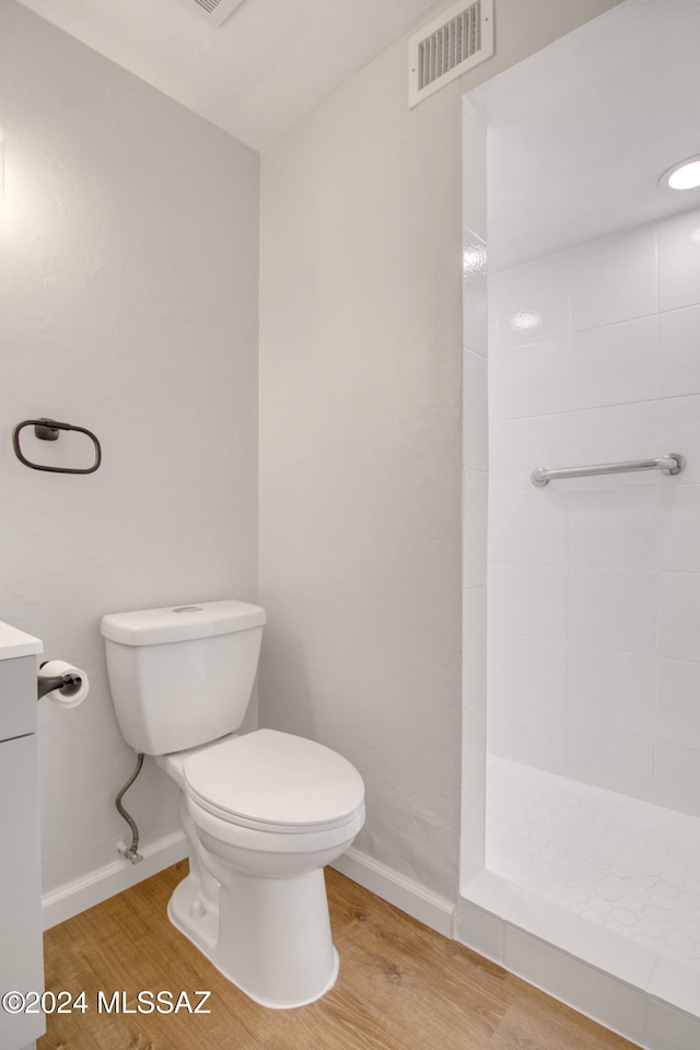 bathroom featuring toilet, wood-type flooring, vanity, and a tile shower