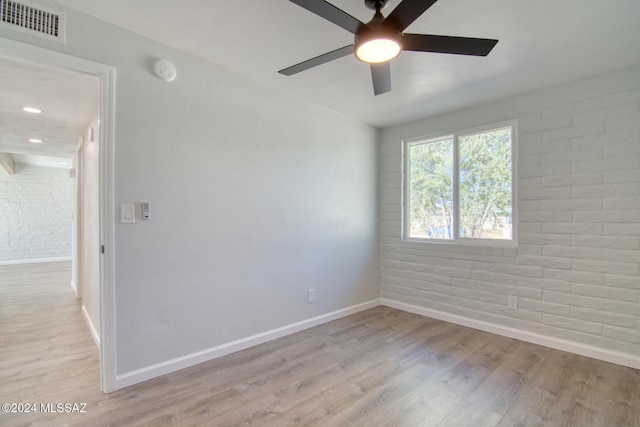 unfurnished room with light wood-type flooring, ceiling fan, and brick wall