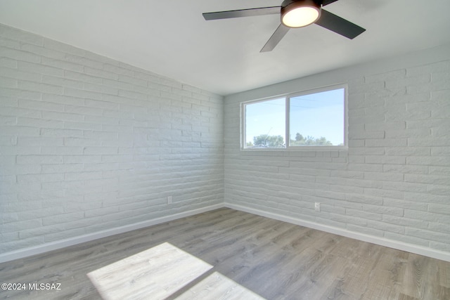 spare room with ceiling fan, light hardwood / wood-style floors, and brick wall