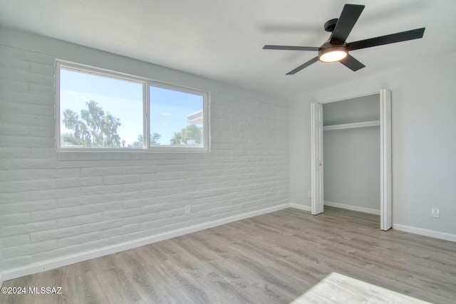 unfurnished bedroom with ceiling fan, light wood-type flooring, brick wall, and a closet