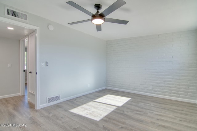 unfurnished room featuring light hardwood / wood-style floors, ceiling fan, and brick wall