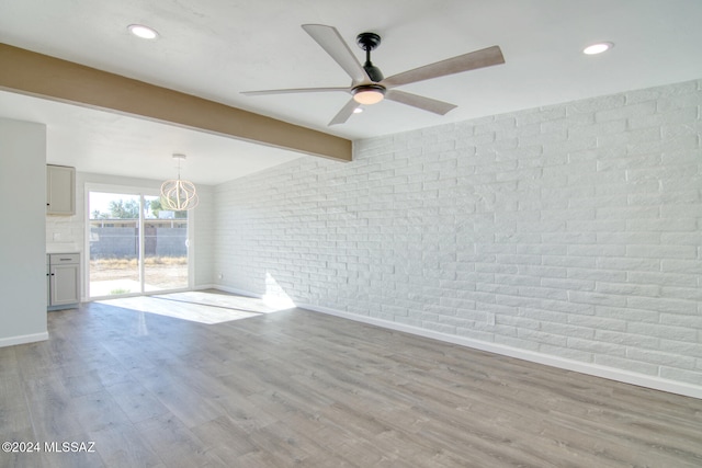 spare room with ceiling fan with notable chandelier, beam ceiling, light wood-type flooring, and brick wall