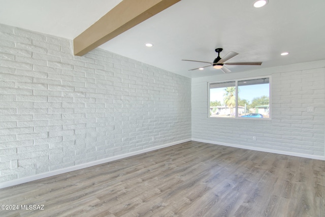 spare room with beam ceiling, light hardwood / wood-style flooring, ceiling fan, and brick wall