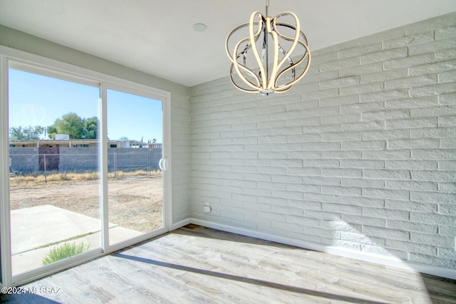 unfurnished dining area featuring a chandelier, hardwood / wood-style flooring, and brick wall