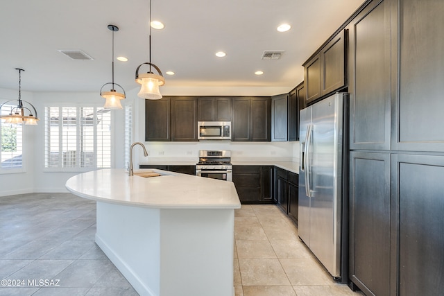 kitchen with stainless steel appliances, dark brown cabinetry, sink, decorative light fixtures, and an island with sink