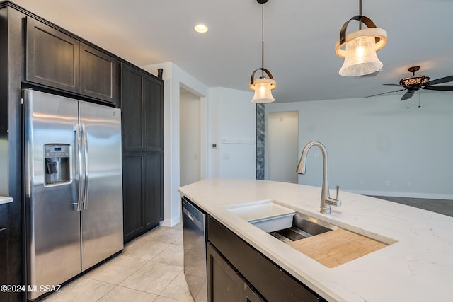 kitchen featuring stainless steel appliances, light stone counters, dark brown cabinetry, sink, and decorative light fixtures