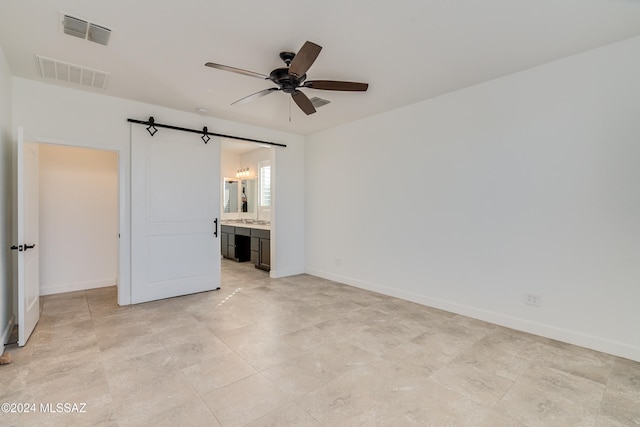 unfurnished bedroom with a barn door, ensuite bathroom, and ceiling fan