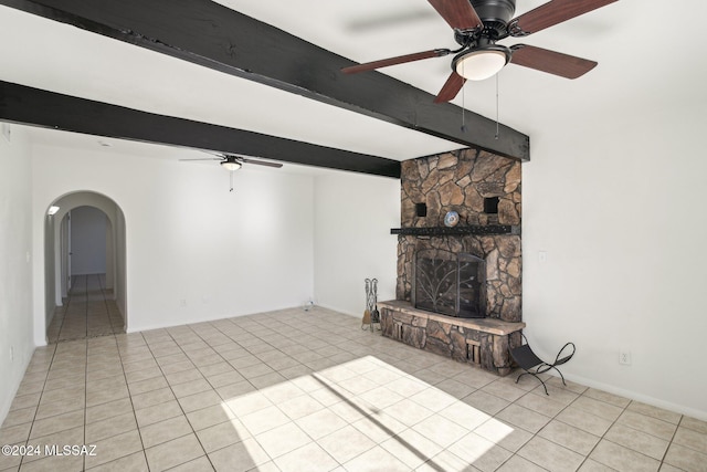 unfurnished living room featuring beam ceiling, a stone fireplace, ceiling fan, and light tile patterned floors