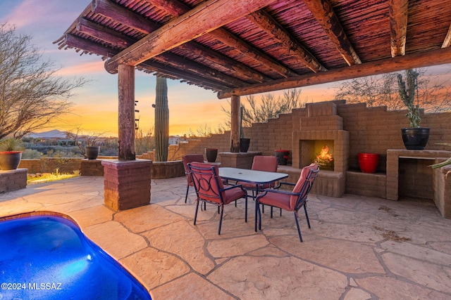 patio terrace at dusk with an outdoor brick fireplace and a fenced in pool