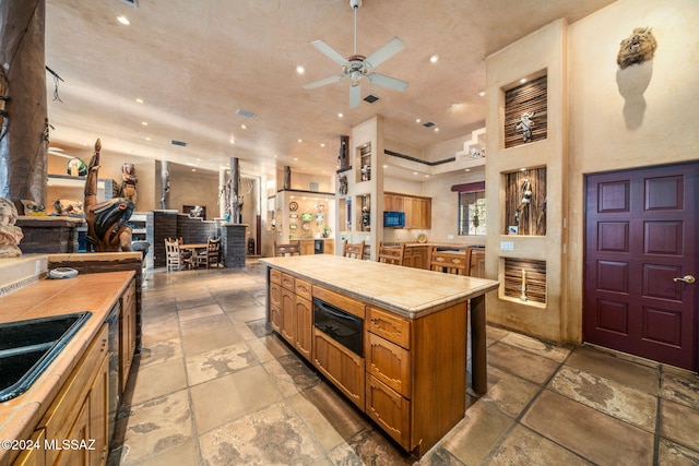 kitchen with tile countertops, sink, ceiling fan, a kitchen island, and a high ceiling