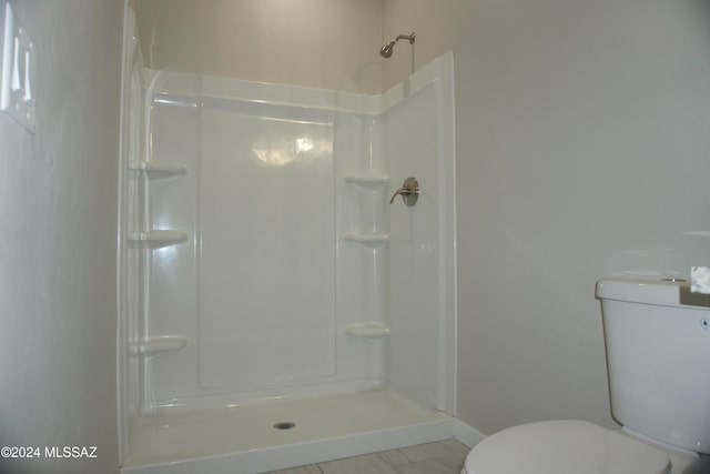 bathroom featuring tile patterned flooring, toilet, and a shower