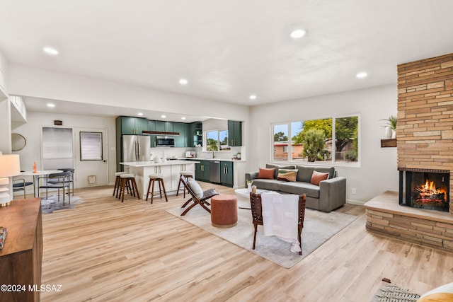 living room featuring a stone fireplace, light hardwood / wood-style flooring, and sink