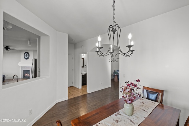 dining area featuring ceiling fan with notable chandelier, a fireplace, baseboards, and wood finished floors