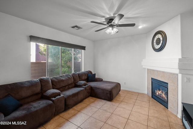 living room with light tile patterned floors, visible vents, a tiled fireplace, a ceiling fan, and baseboards