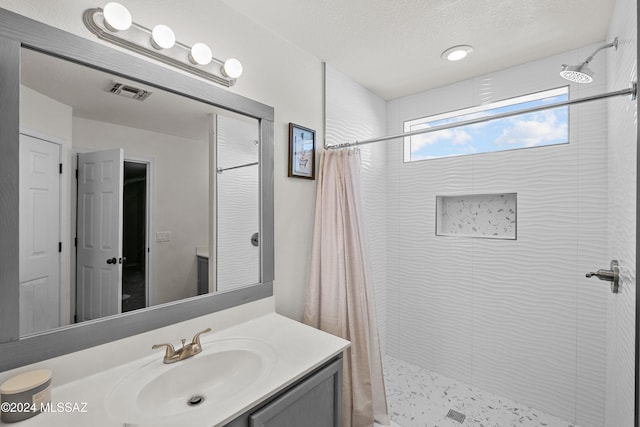 bathroom with visible vents, a tile shower, a textured ceiling, and vanity