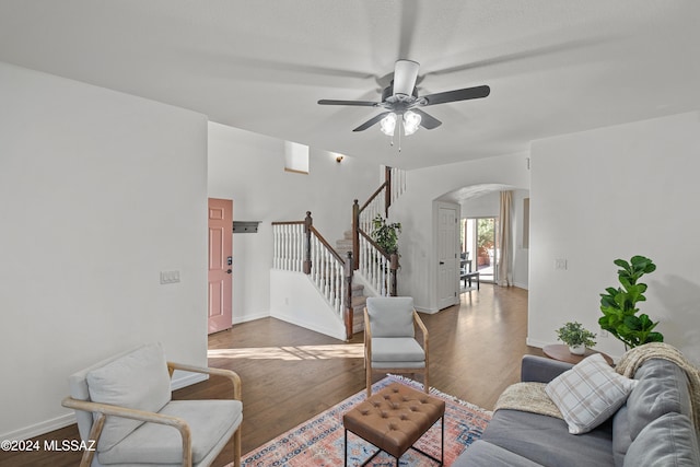 living area featuring arched walkways, wood finished floors, a ceiling fan, baseboards, and stairs