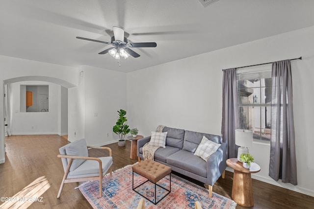 living room with arched walkways, wood finished floors, a ceiling fan, and baseboards