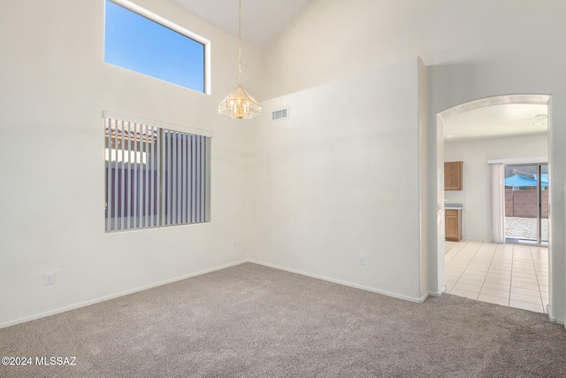 empty room featuring high vaulted ceiling, a chandelier, and light carpet