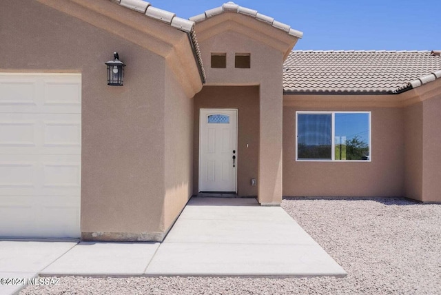 view of exterior entry featuring a tiled roof, an attached garage, and stucco siding