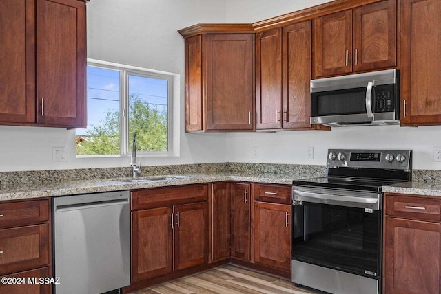 kitchen with sink, stainless steel appliances, light hardwood / wood-style floors, and light stone countertops