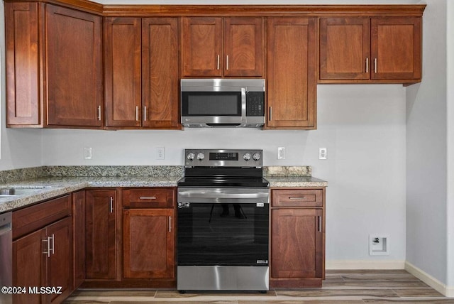 kitchen with stainless steel appliances, light stone countertops, and light hardwood / wood-style flooring