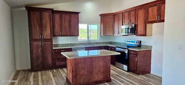 kitchen featuring a kitchen island, sink, light hardwood / wood-style floors, stainless steel appliances, and light stone countertops