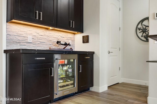 bar featuring light wood-type flooring, wine cooler, and tasteful backsplash