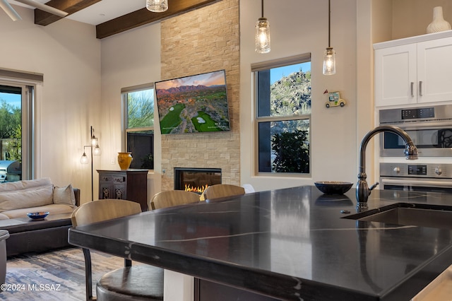 kitchen with a high ceiling, hanging light fixtures, a fireplace, beam ceiling, and white cabinetry