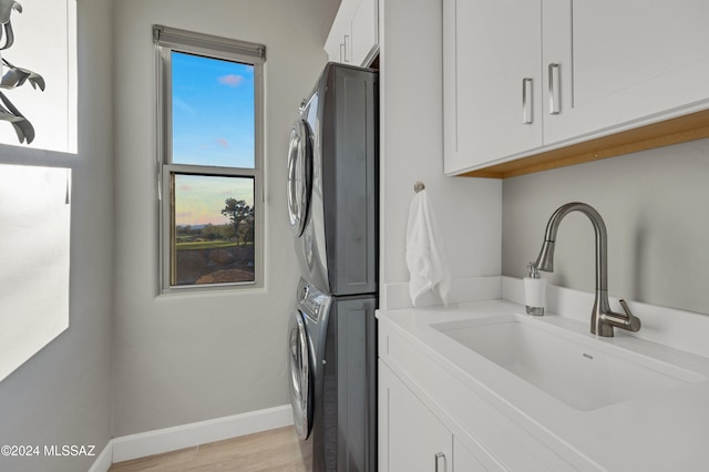 washroom featuring sink, cabinets, light hardwood / wood-style flooring, and stacked washer and clothes dryer