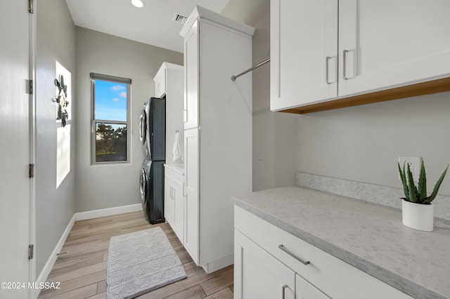 laundry room with cabinets, light hardwood / wood-style flooring, and stacked washer / dryer