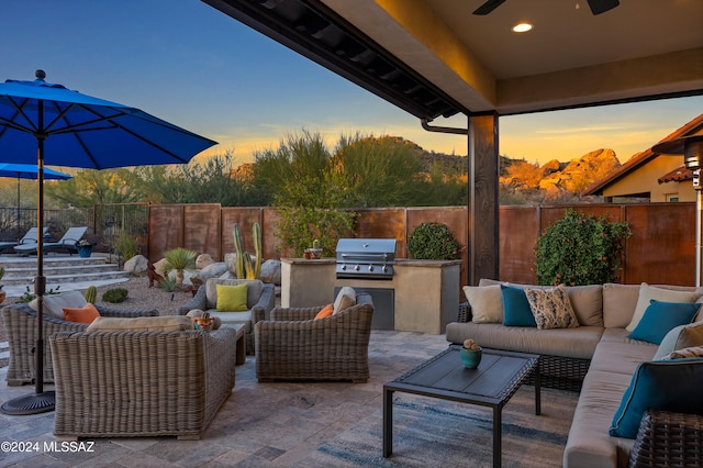 patio terrace at dusk featuring an outdoor living space, an outdoor kitchen, grilling area, and ceiling fan