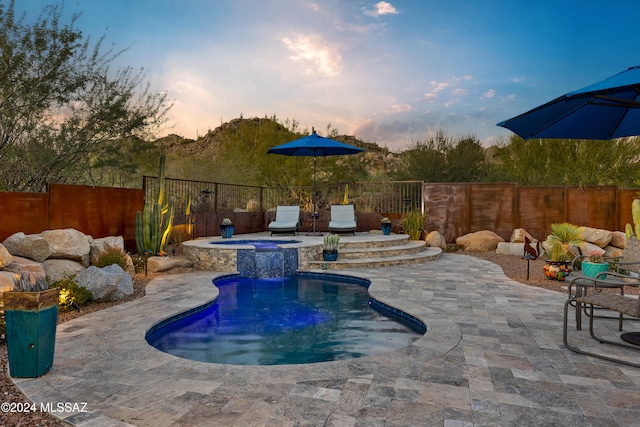 pool at dusk with an in ground hot tub and a patio