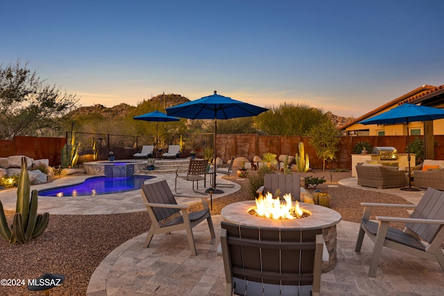 patio terrace at dusk with a pool with hot tub, an outdoor living space with a fire pit, and a grill