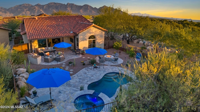 exterior space with an in ground hot tub, a mountain view, a patio, and an outdoor living space with a fire pit