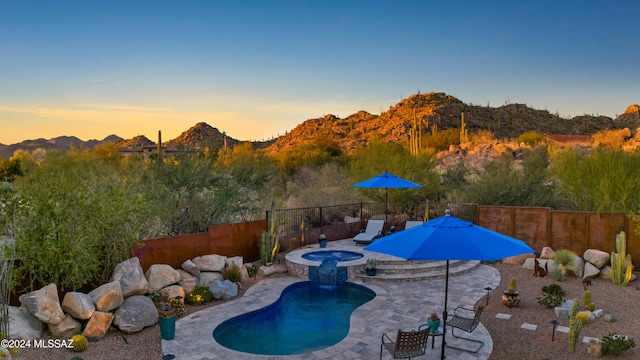 pool at dusk with a patio area, an in ground hot tub, and a mountain view