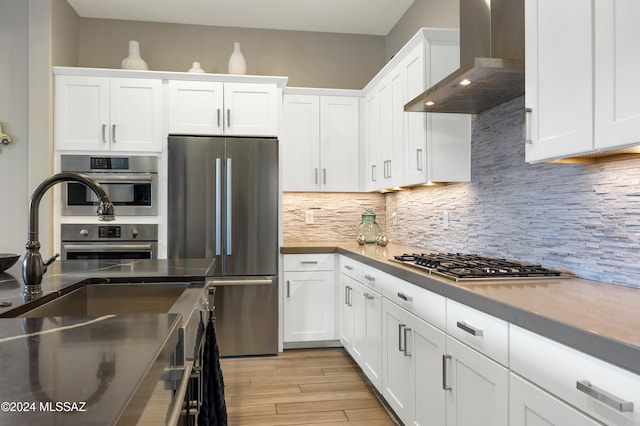 kitchen featuring white cabinets, light hardwood / wood-style floors, wall chimney range hood, and stainless steel appliances