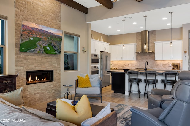 living room featuring beam ceiling, a stone fireplace, light wood-type flooring, and sink