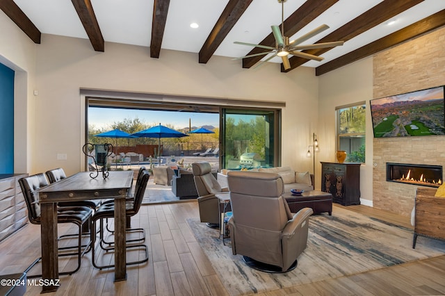 living room featuring ceiling fan, a stone fireplace, beamed ceiling, high vaulted ceiling, and wood-type flooring