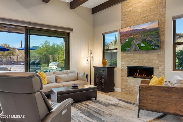 living room featuring beam ceiling, a fireplace, light hardwood / wood-style flooring, and high vaulted ceiling