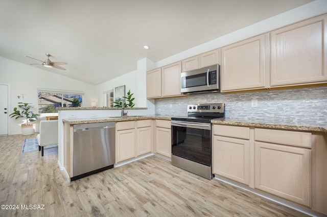 kitchen featuring lofted ceiling, kitchen peninsula, sink, light wood-type flooring, and appliances with stainless steel finishes