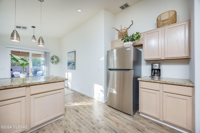 kitchen with light hardwood / wood-style floors, stainless steel refrigerator, light brown cabinetry, and pendant lighting